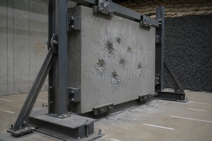 A concrete test panel in a steel test frame showing ballistic impacts