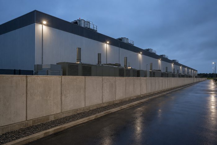 Precast concrete perimeter wall along a data center at dusk, with generator and switchgear enclosures behind it