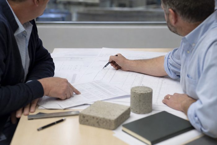 Two people reviewing a project requirement and drawings at a table, with cut concrete cylinder and cast block samples in front of them