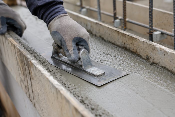 A finisher working the surface of fresh concrete in a wall form with a steel trowel