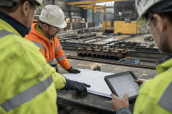 A plant manager in a hi-vis vest and hard hat surveying long precast casting beds in a production hall at first light