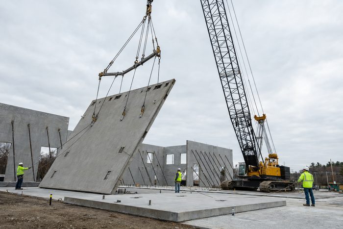A large precast concrete wall panel being lifted from horizontal to vertical by a crawler crane on a tilt-up site